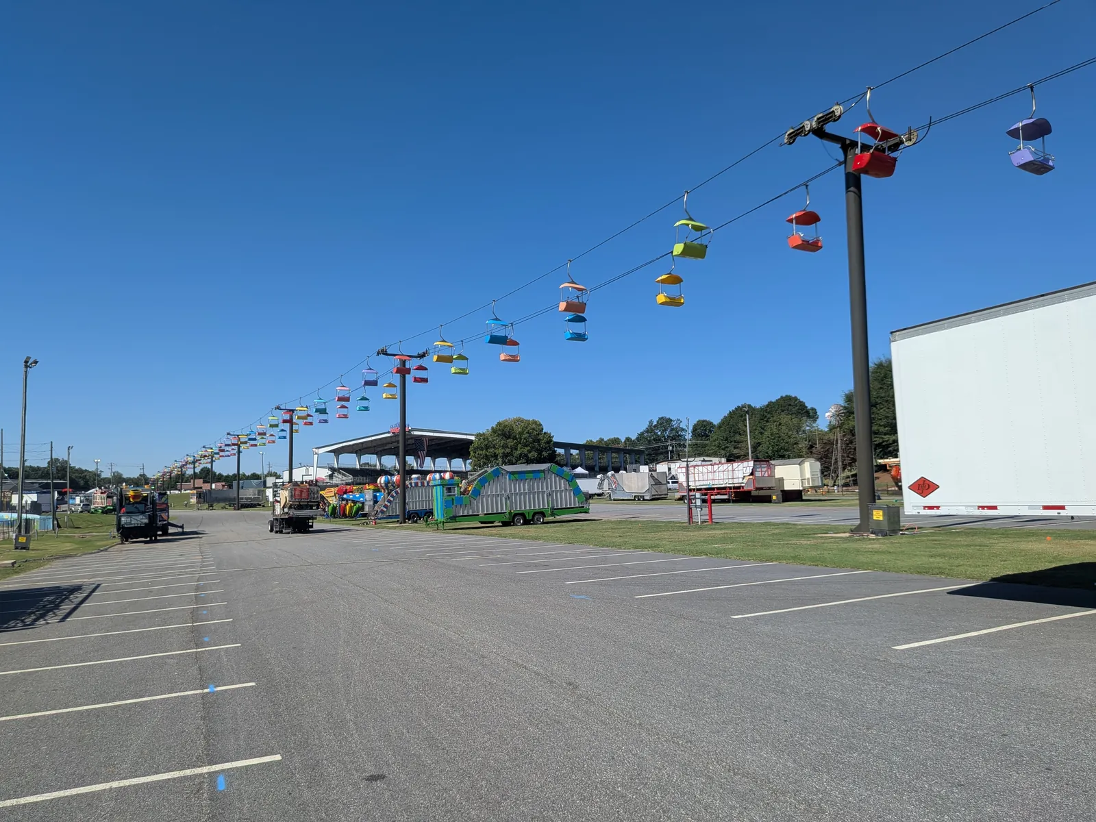 A wide view across an empty parking lot toward the line of sky-ride chairs, with trailers and ride equipment parked along the midway.
