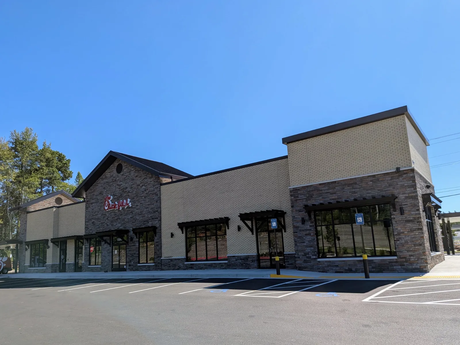 A brick-and-stone Chick-fil-A restaurant with its red script sign, dark-framed windows and an empty, freshly striped parking lot.